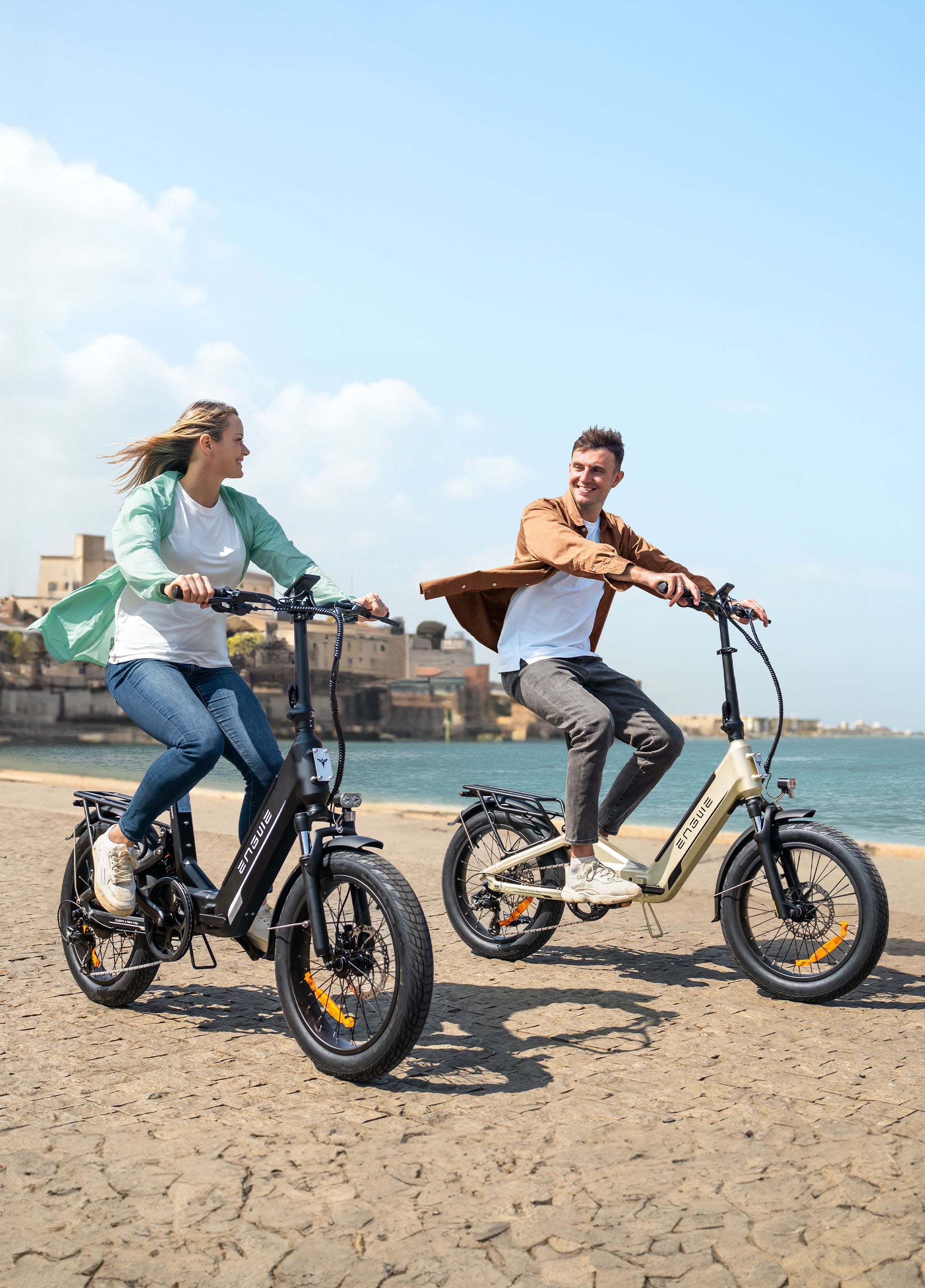 Two riders enjoying the ENGWE L20 3.0 Boost electric bikes by the waterfront on a sunny day.